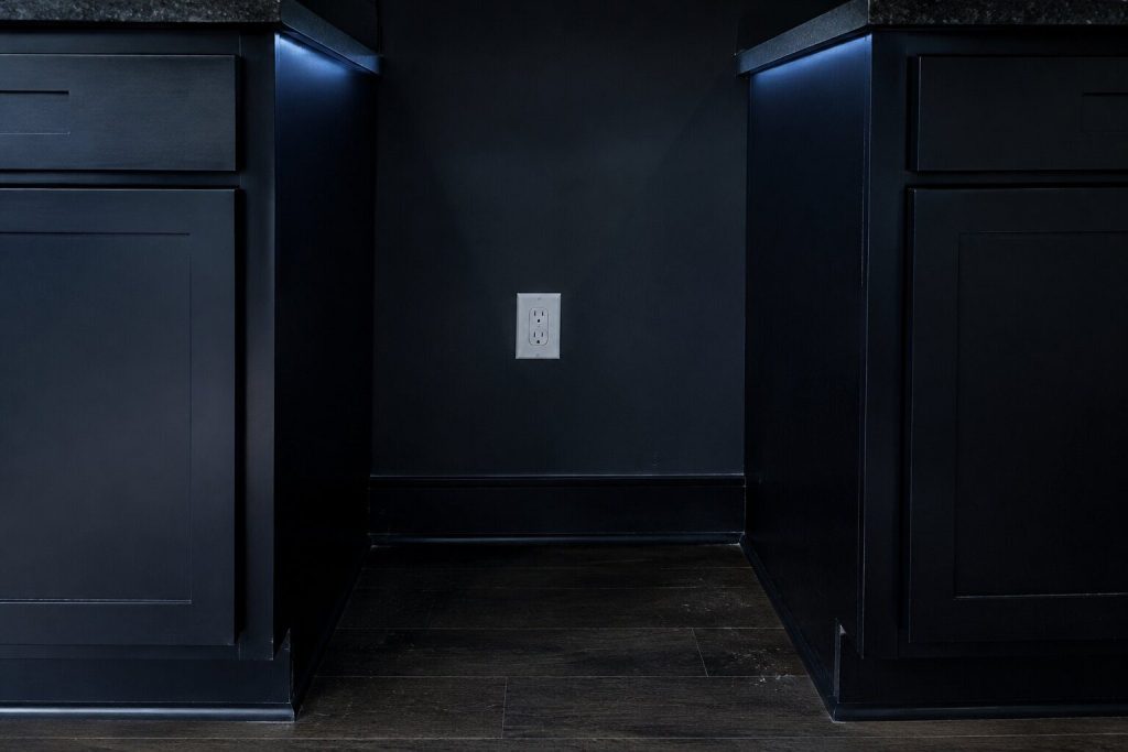The empty rectangular gap left between two dark base cabinets where an appliance has been taken out, the bare wall and its outlet visible at the back