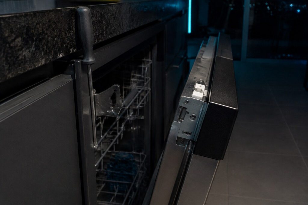 The latch at the top of a dishwasher door and the strike it closes into, the door held an inch open so both halves read. A latch that reports open intermittently is the machine that sometimes runs and sometimes does not.