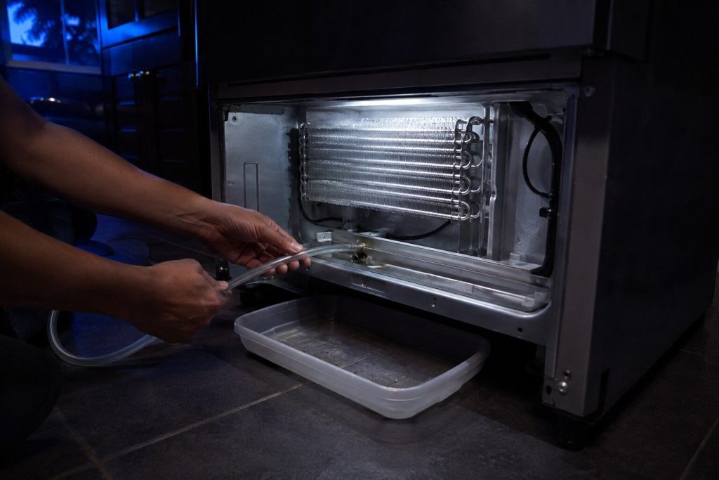 Flexible tubing fed into the drain trough at the bottom of an evaporator compartment with a tray under the machine. The blocked defrost drain is the cause of most water under the crispers, which is what this page is called out to.