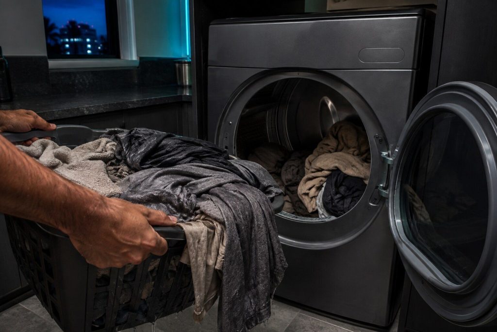 A basket lifted out of a dryer whose contents still hang heavy and damp with the drum behind half loaded. Everything came out warm and wet, which is the complaint in one frame rather than a duct nobody can see.